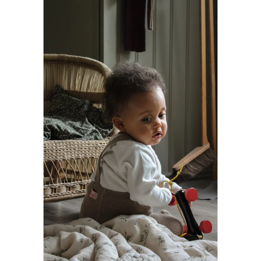 Kleinkind sitzt auf dem Boden und hält ein Spielzeug, trägt Strumpfhose mit Träger