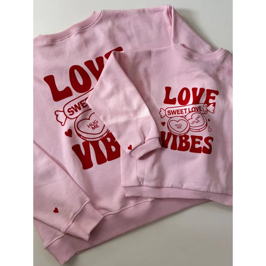 Zwei pinke Sweatshirts mit Love Vibes-Text und roten Herzdesigns von Blossom