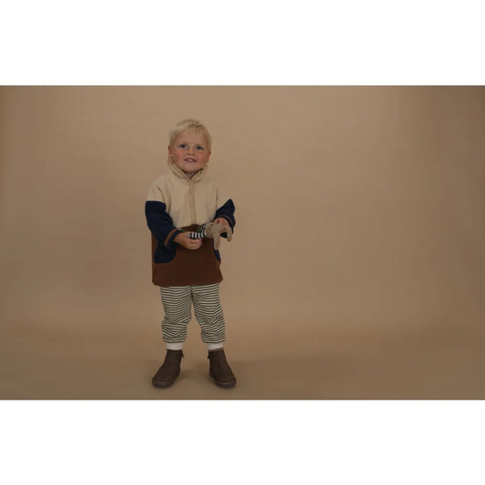 Junges Kind mit Farbblock-Hoodie, gestreiften Hosen und braunen Stiefeln hält Stofftier