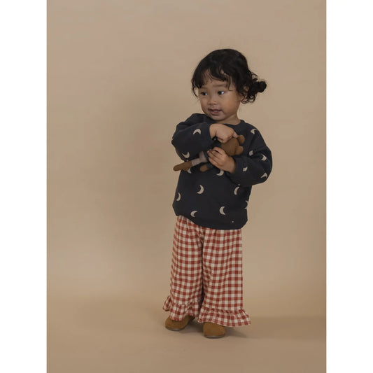 Kleines Kind in dunkelblauem Mond-Print Oberteil und roten Gingham-Hosen mit Rüschensaum