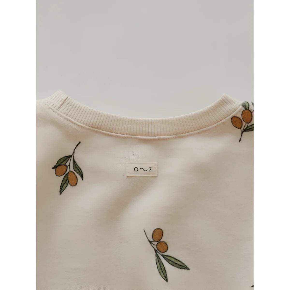 Cremefarbener Pullover mit einem Muster aus Olivenzweigen und Früchten