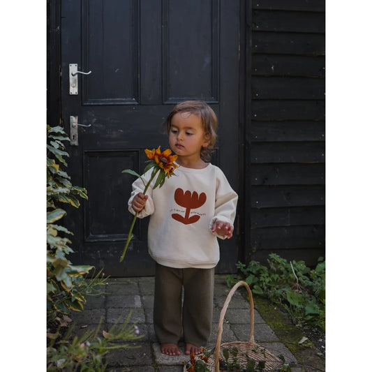 Ein Kind in einem weißen Sweatshirt mit Blumenmuster riecht an einer Sonnenblume