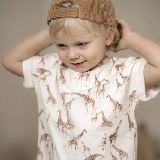 Junges Kind in weißem T-Shirt mit Giraffenmuster und beiger Cordmütze