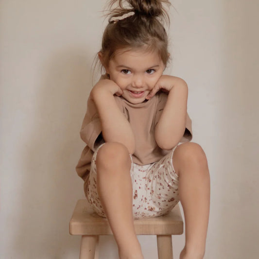 Lächelndes Kleinkind auf Hocker trägt T-Shirt von Kakao