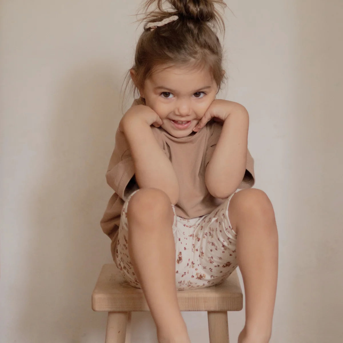 Lächelndes Kleinkind auf Hocker trägt T-Shirt von Kakao