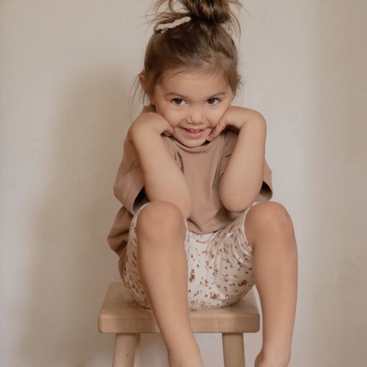 Lächelndes Kleinkind auf Hocker trägt T-Shirt von Kakao