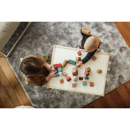 Zwei Kinder spielen mit Korkbausteinen auf einer weißen Matte