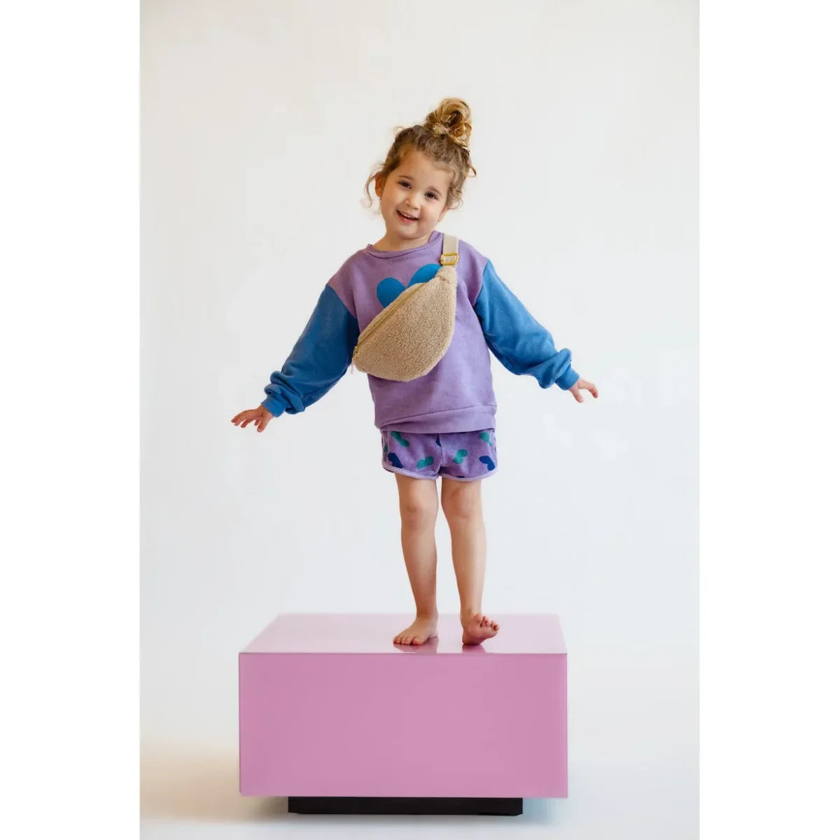 Lächelndes Mädchen in bunter Kleidung mit Teddy Mini Gürteltasche in Ecru