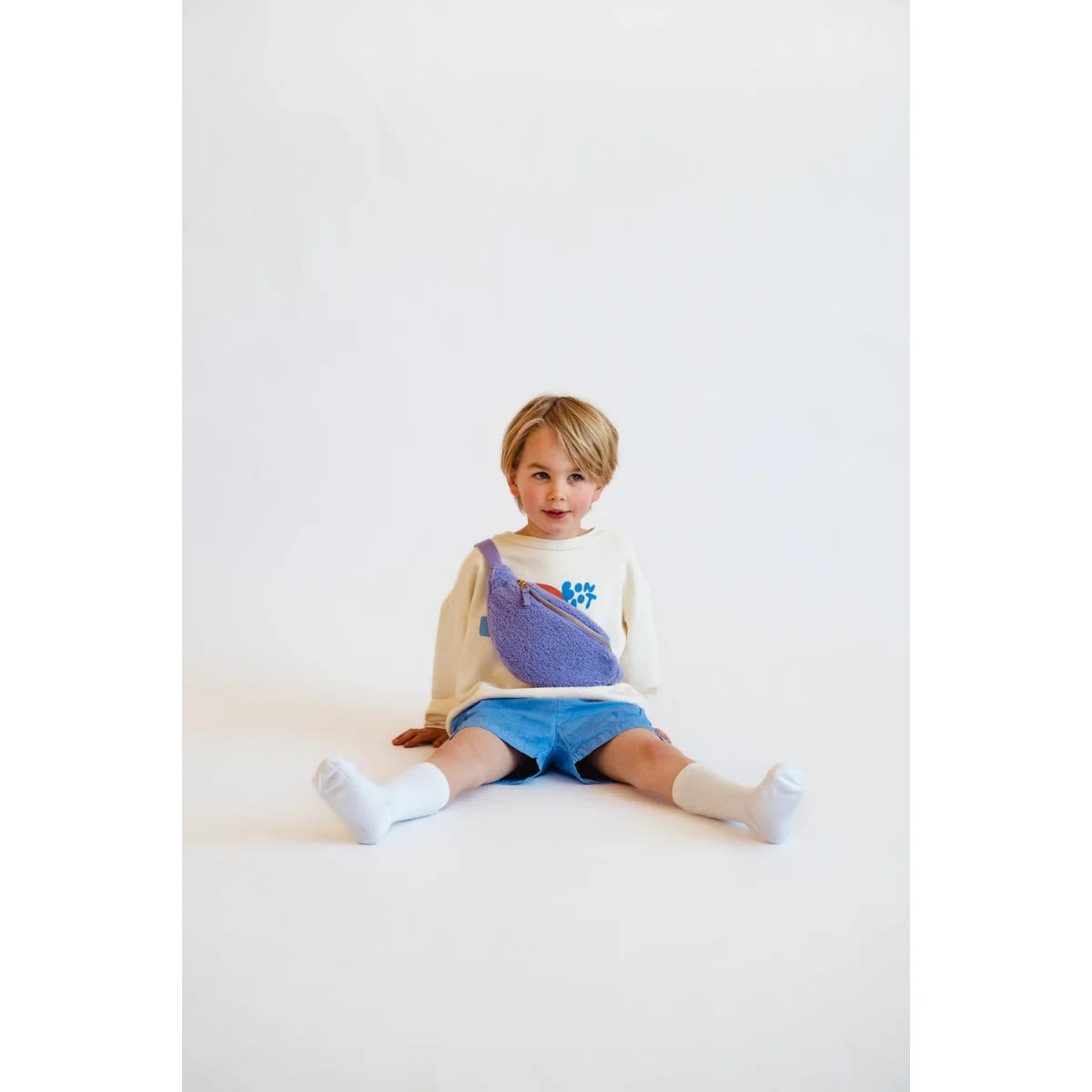 Junge sitzt auf dem Boden in buntem Outfit mit Teddy Mini Fanny Pack in Lila