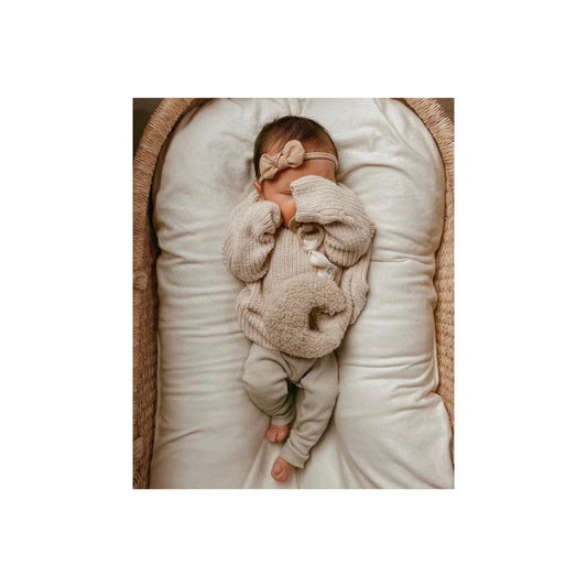 Schlafendes Neugeborenes in einem gestrickten Overall und Haarband in Beige