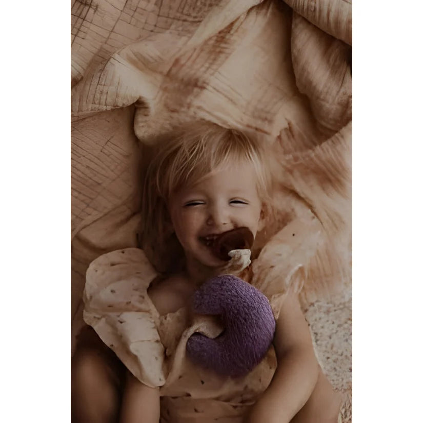 Lachendes Baby mit lila Stofftier auf Stoff, Produkt Teddy Mond | Purple Rain