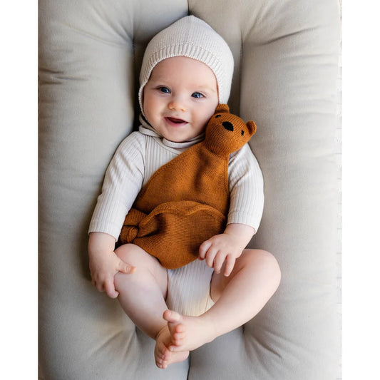Lächelndes Baby mit einem gestrickten Bären in Rust-Ton von Teddy Tokki