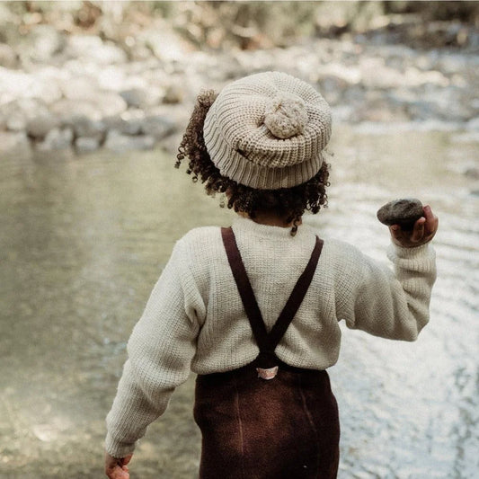 Kind mit Strumpfhosen und Mütze hält einen Stein am Bach in der Natur