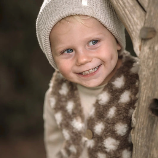 Lächelndes Kind mit weißer Mütze und gepunkteter Jacke von Teddyplüsch