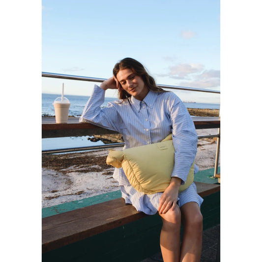 A butter yellow textured puffy cross body bag with a soft quilted surface and a small rectangular front patch