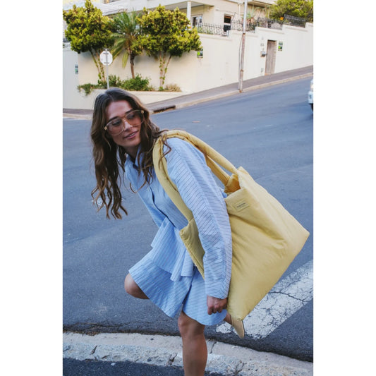 Gelbe canvas tote bag mit stabilen griffen und kleinem logo-patch seitlich aus buttergelbem texturiertem material