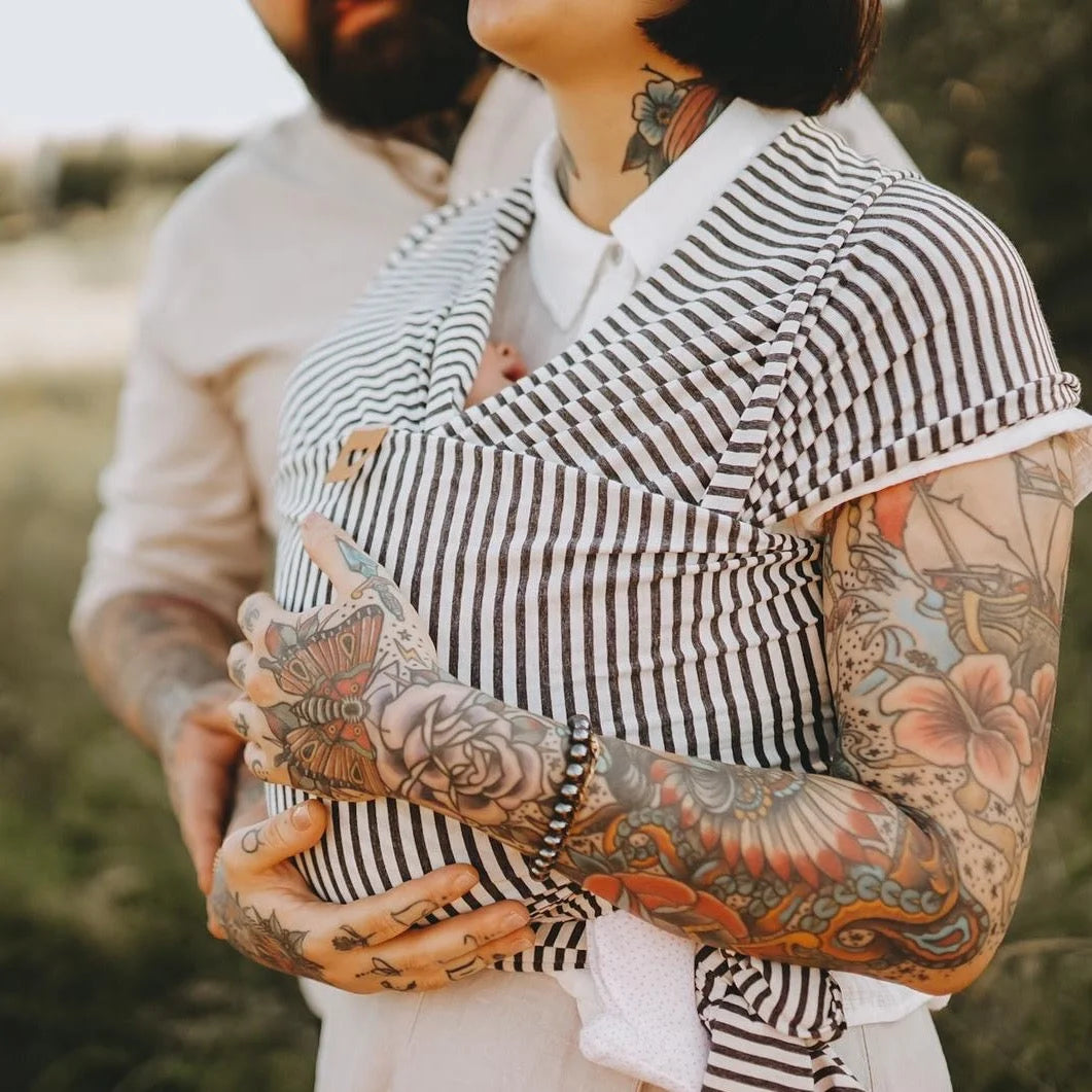 Schwarz-weiß gestreifter Babytrage mit bunttätowierten Armen im Einsatz