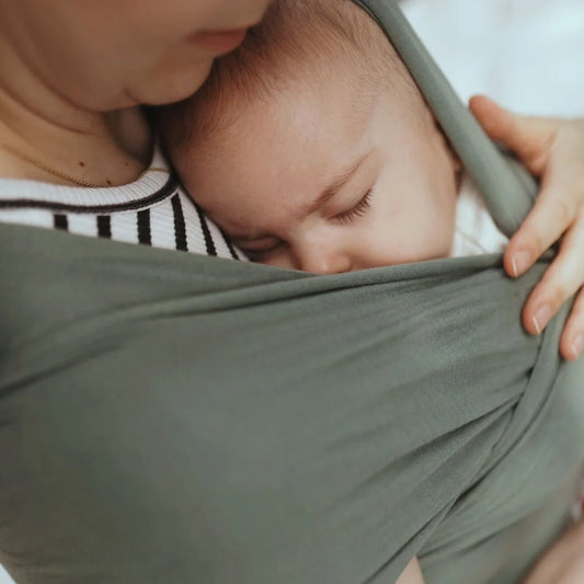 Baby schläft friedlich in einem salbeigrünen Tragetuch in Waldgrün