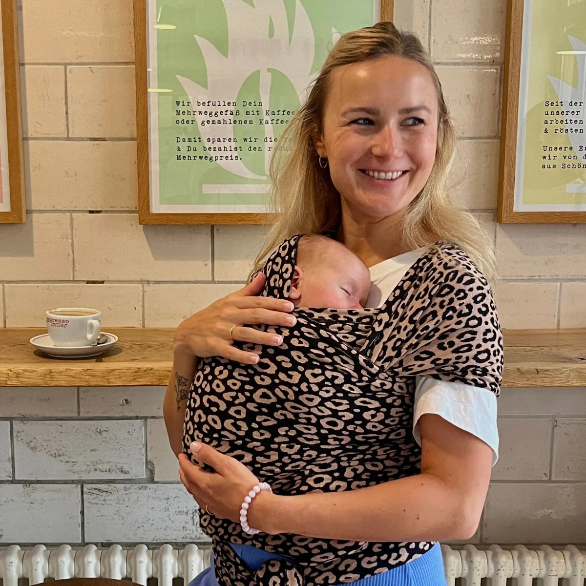 Eine Mutter mit Leopardenmuster-Tragetuch trägt ihr schlafendes Baby