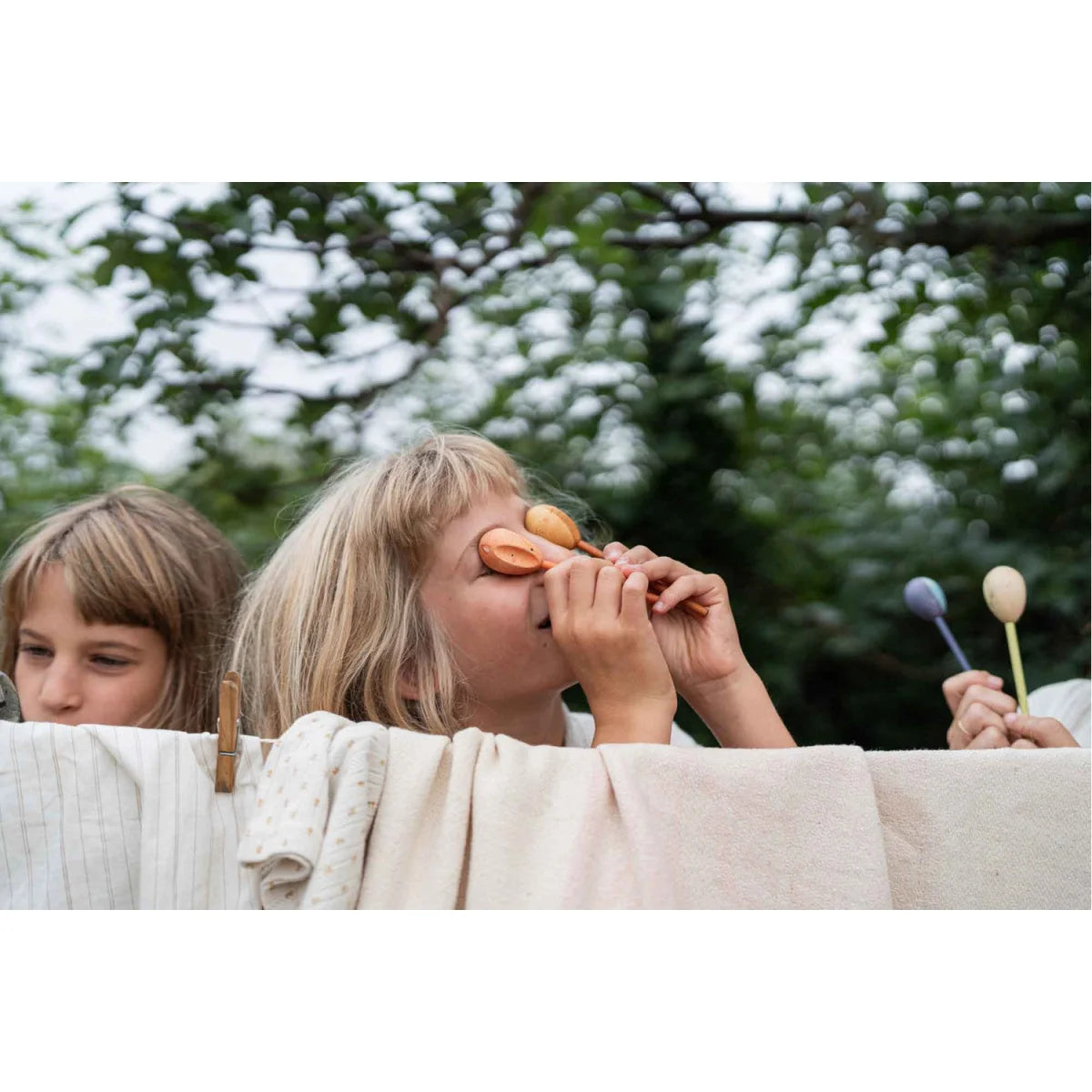 Kind hält hölzernes Maraca mit glatter hellbrauner Oberfläche und runden Enden von Twin-souls Puppets