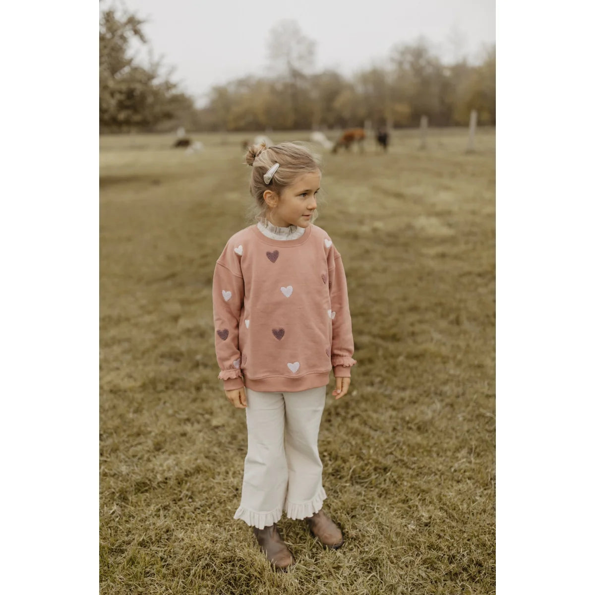 Junge Mädchen in dusty rose Sweatshirt mit Herz, Rüschenhose und braunen Stiefeln