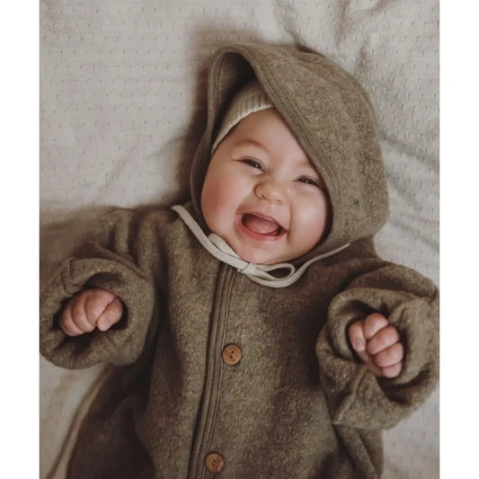 Ein fröhliches Baby in einem kuscheligen, braunen Kapuzenmantel mit Knöpfen