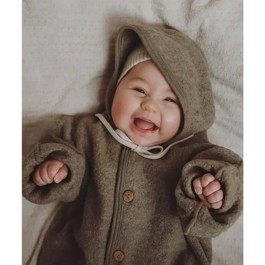 Ein fröhliches Baby in einem kuscheligen, braunen Kapuzenmantel mit Knöpfen