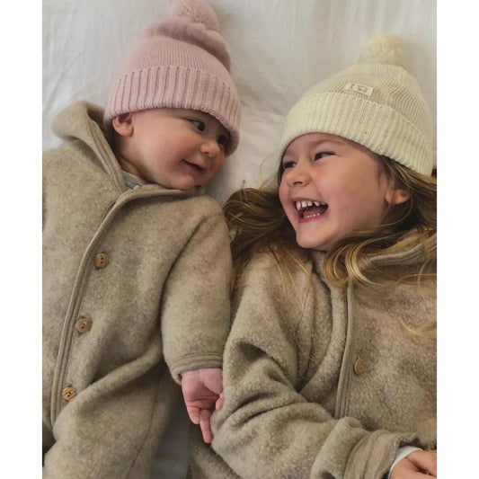 Zwei Kinder in beigen Mänteln und Wintermützen genießen einen fröhlichen Moment