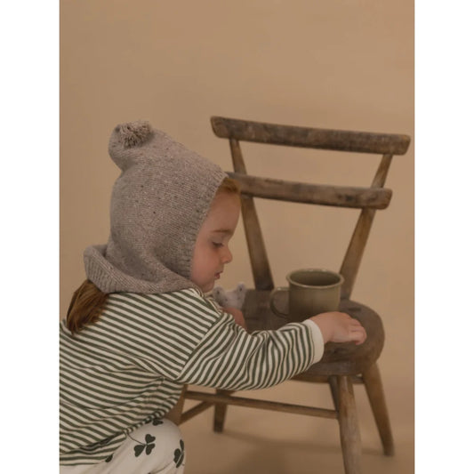 Kindliches Kind trägt eine gestrickte Mütze mit Bommel aus Wolle Oatmeal