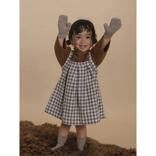 Lächelndes Kleinkind in braunem Langarmshirt, blauer Kittelschürze und grauen Handschuhen