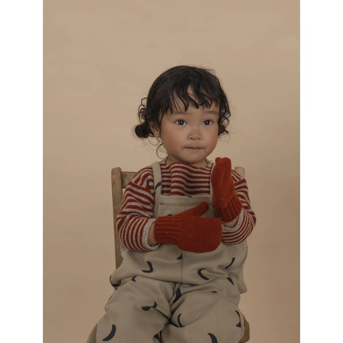 Kleines Baby mit rotem und weißem gestreiftem Pullover und beige Overalls