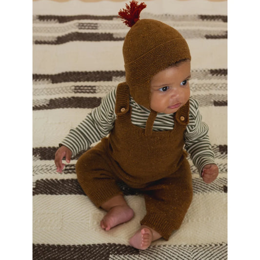 Niedliches Baby trägt braune Strickmütze mit rotem Zopf und passende Overalls