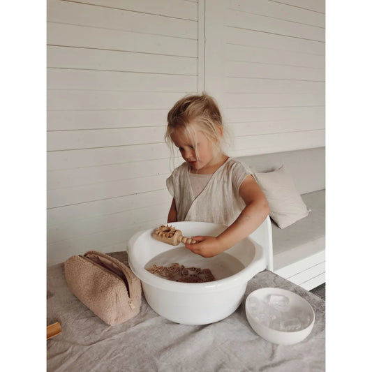 Junges Kind spielt mit einem weißen Plastikschaufelchen gefüllt mit Wasser und Sand