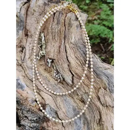 Perlenkette mit goldfarbener Schließe auf verwittertem Holz präsentiert.