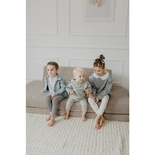 Drei junge Kinder unterschiedlichen Alters sitzen nebeneinander auf einer weichen, modularen Couch