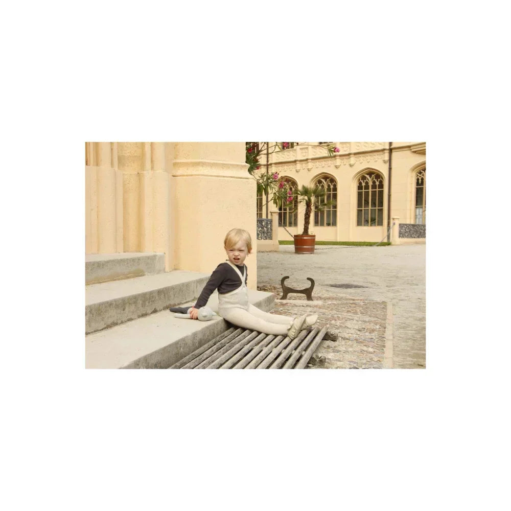 Kind sitzt in Latzhose auf einem Gitter in der nachhaltigen Kindermode.