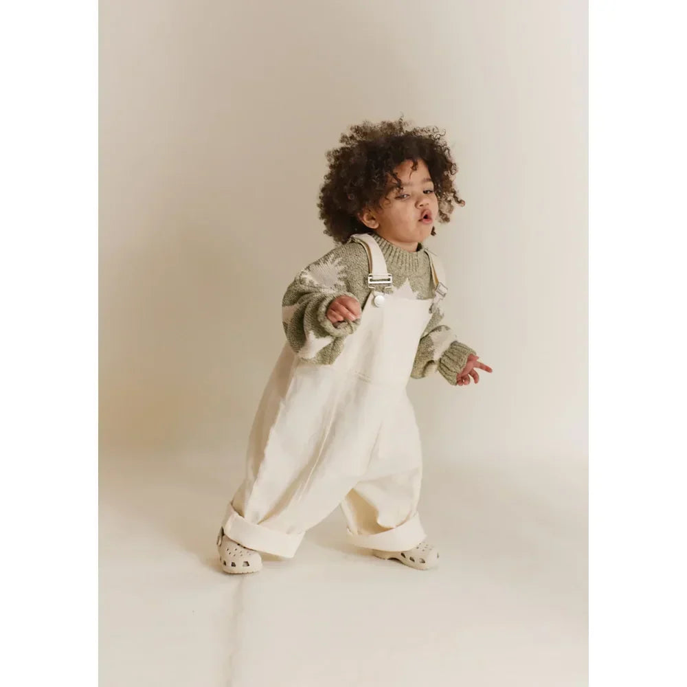 Kleinkind in hellgrün gestricktem Pullover und weißen Latzhosen bei Littlies + Mums