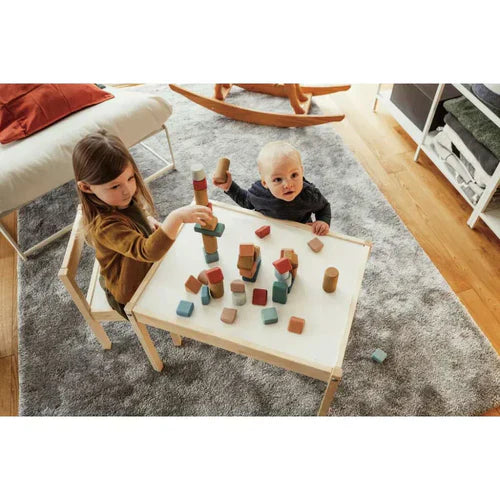 Zwei Kinder spielen mit Holzbausteinen auf einem weißen Tisch.