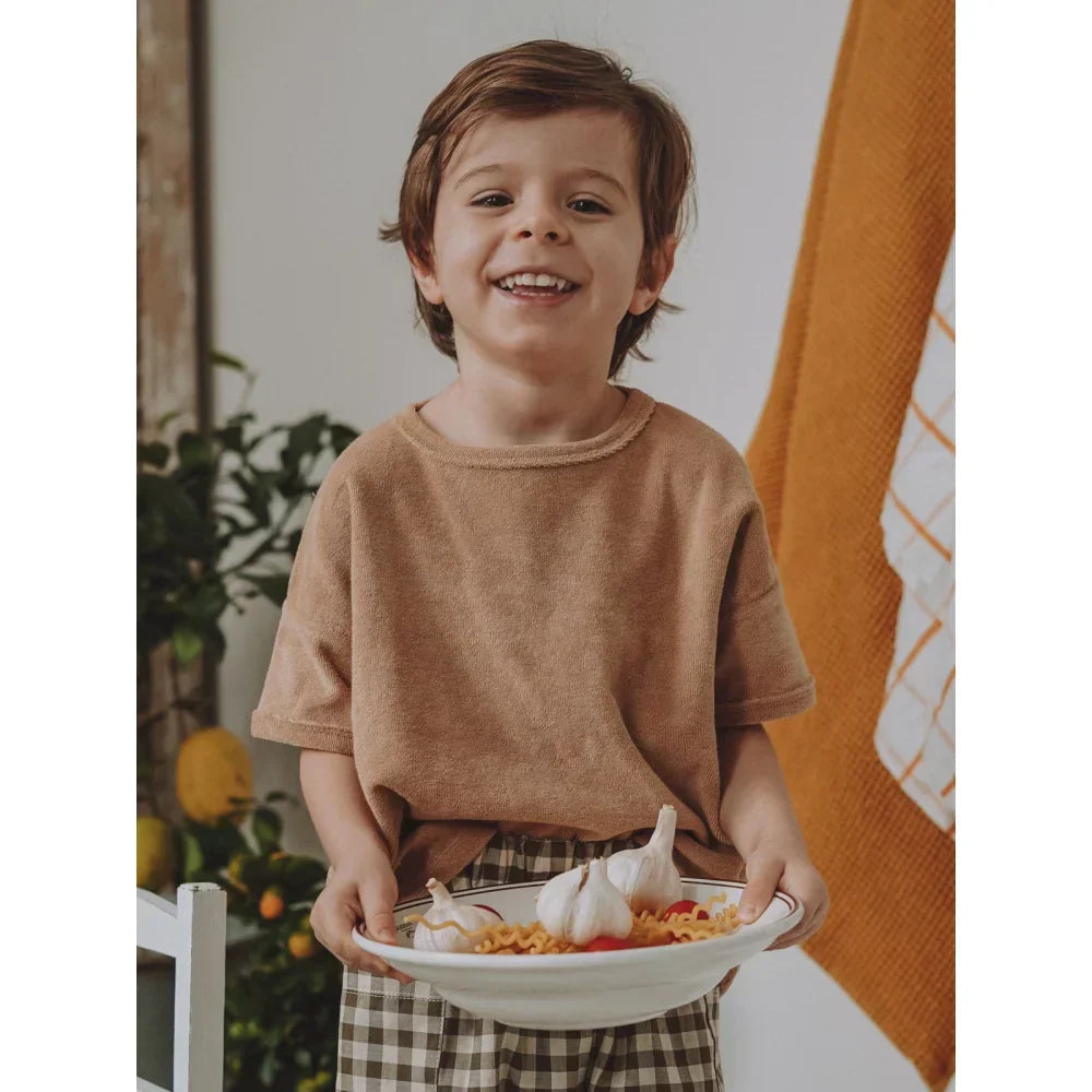 Lächelndes Kind hält eine Schüssel mit Essen in der natürlichen Kindermode.