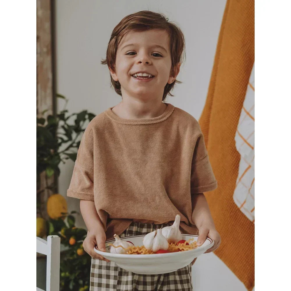 Lächelndes Kind hält eine Schüssel mit Essen in der natürlichen Kindermode.
