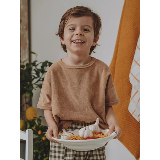 Lächelndes Kind hält eine Schüssel mit Essen in der natürlichen Kindermode.