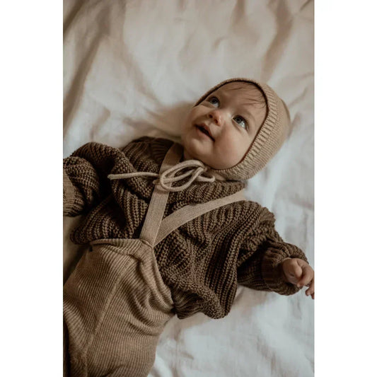 Baby in einem gemütlichen braunen Strickpullover und passender Mütze.
