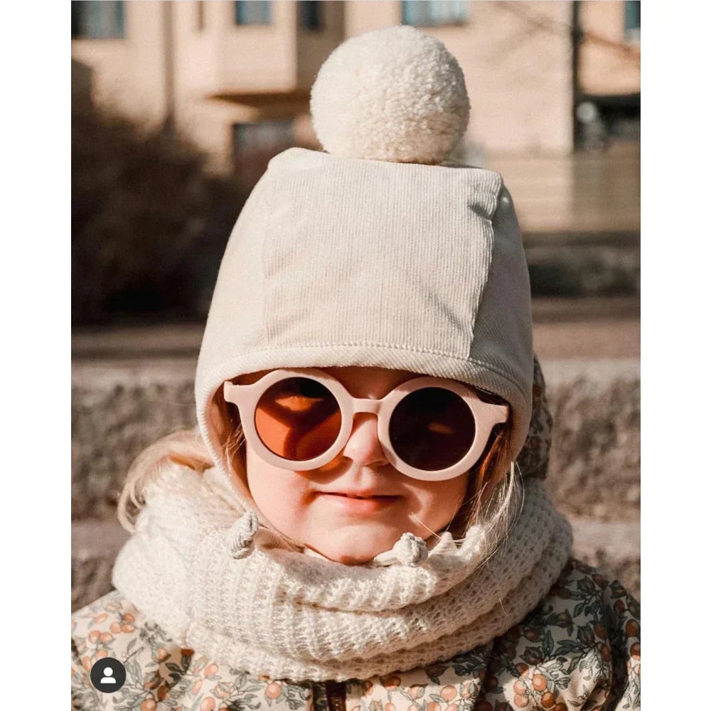 Kindergesicht mit hellfarbenem Bommelmütze, runden Sonnenbrillen und gemusterter Jacke