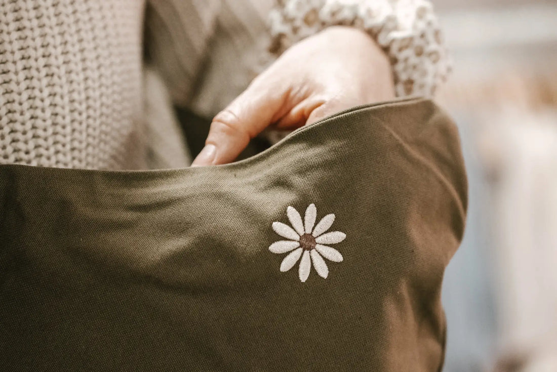 Olivgrüner Stoff mit einem weißen Gänseblümchen-Stickdesign für Kindertragen.