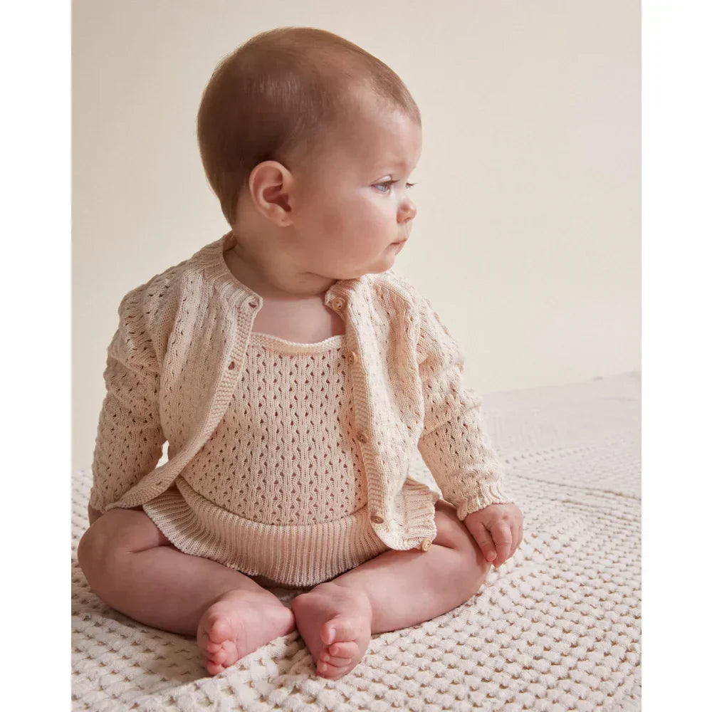 Baby im gestrickten Overall und Cardigan in zeitloser Kindermode für Fashionistas.