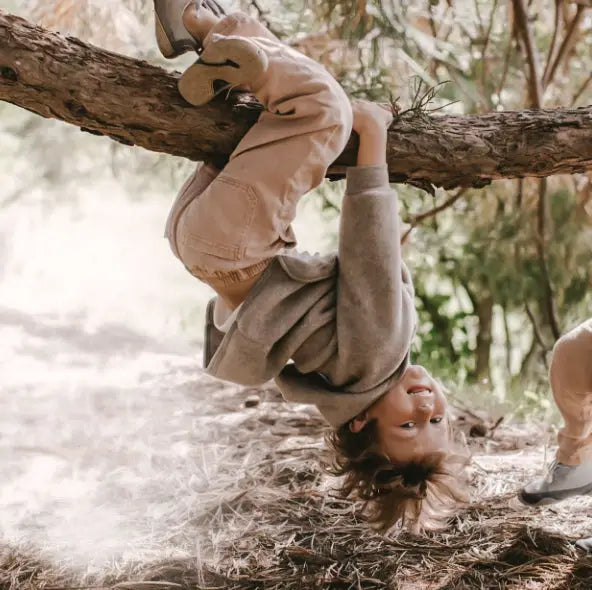 Kind eines Kindes, das spielerisch kopfüber an einem Baum hängt, Teil der ENGEL NATUR Sammlung