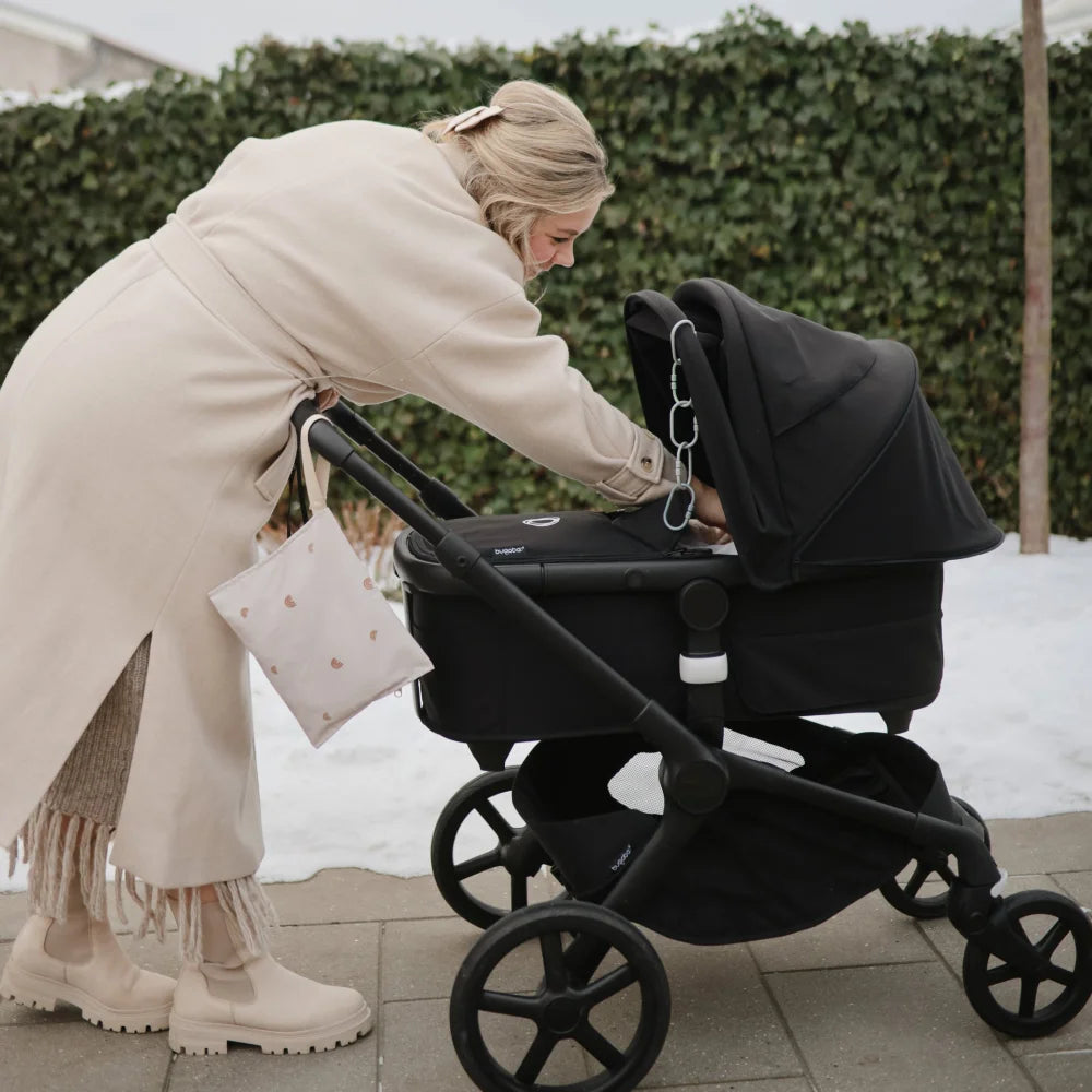 Schwarzer Kinderwagen, geschoben von einer Person im cremefarbenen Mantel