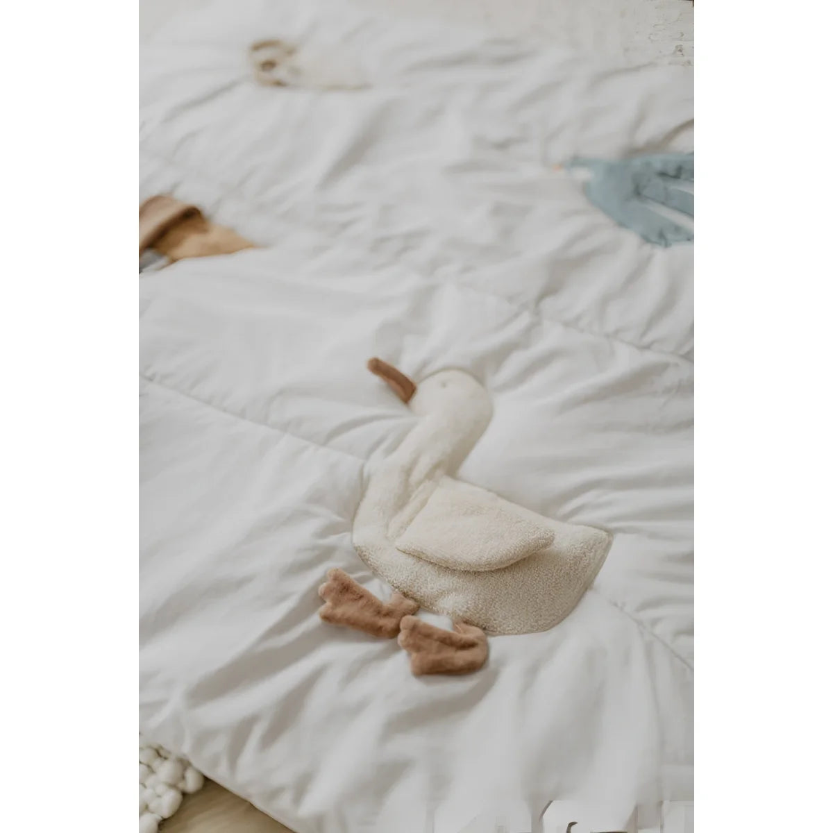 A weiche cremefarbene plüschente mit braunen füßen und schnabel auf weißer gesteppter activity decke für nachhaltige babykleidung schweiz