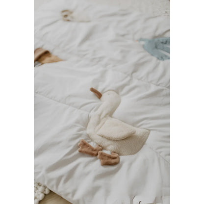 A weiche cremefarbene plüschente mit braunen füßen und schnabel auf weißer gesteppter activity decke für nachhaltige babykleidung schweiz