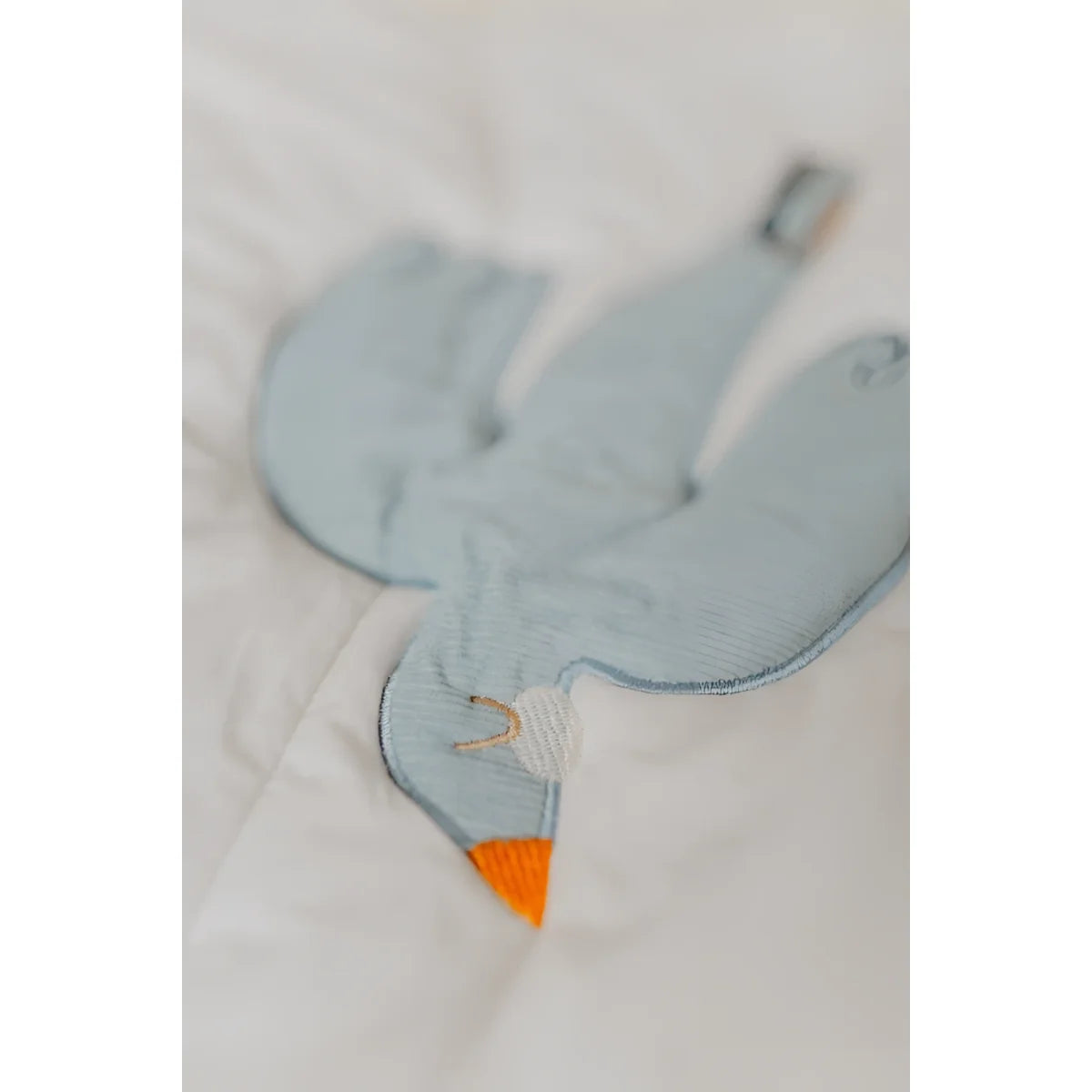 Ein soft hellblauer gestickter vogel-förmiger plüsch mit orangefarbenem schnabel auf einer activity decke für nachhaltige babykleidung schweiz